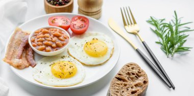 Yağda yumurta, pastırma, fasulye, domates, baharat ve bitkilerle İngiliz kahvaltısı. Güne doyurucu ve doyurucu bir başlangıç.