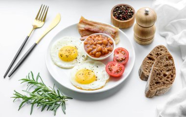Yağda yumurta, pastırma, fasulye, domates, baharat ve bitkilerle İngiliz kahvaltısı. Güne doyurucu ve doyurucu bir başlangıç.
