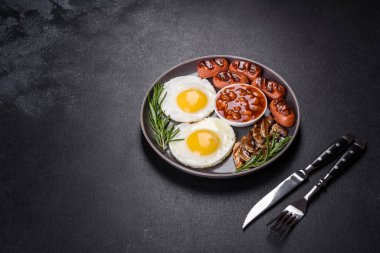 Tam İngiliz kahvaltısı. Fasulye, sahanda yumurta, kızarmış sosis, domates, mantar. Koyu beton bir masada kızarmış ekmek.