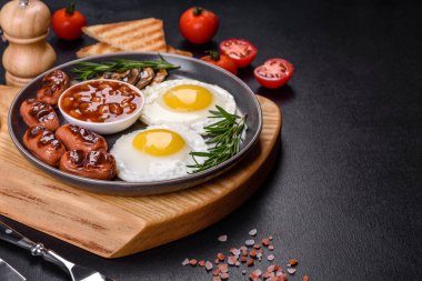 Tam İngiliz kahvaltısı. Fasulye, sahanda yumurta, kızarmış sosis, domates, mantar. Koyu beton bir masada kızarmış ekmek.