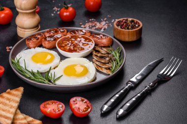 Tam İngiliz kahvaltısı. Fasulye, sahanda yumurta, kızarmış sosis, domates, mantar. Koyu beton bir masada kızarmış ekmek.