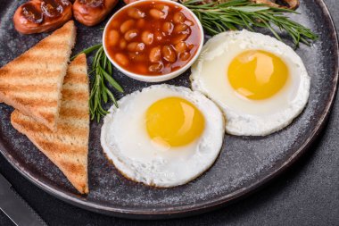 Tam İngiliz kahvaltısı. Fasulye, sahanda yumurta, kızarmış sosis, domates, mantar. Koyu beton bir masada kızarmış ekmek.