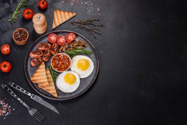 Tam İngiliz kahvaltısı. Fasulye, sahanda yumurta, kızarmış sosis, domates, mantar. Koyu beton bir masada kızarmış ekmek.