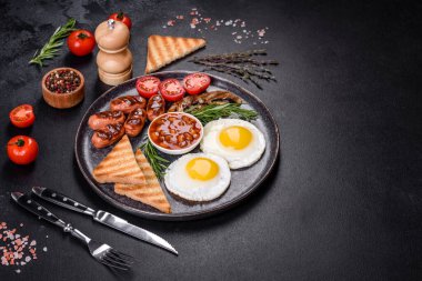 Tam İngiliz kahvaltısı. Fasulye, sahanda yumurta, kızarmış sosis, domates, mantar. Koyu beton bir masada kızarmış ekmek.