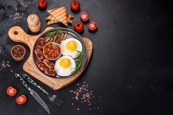 Tam İngiliz kahvaltısı. Fasulye, sahanda yumurta, kızarmış sosis, domates, mantar. Koyu beton bir masada kızarmış ekmek.