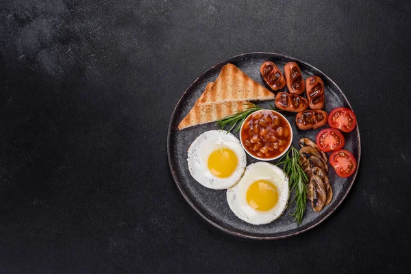 Tam İngiliz kahvaltısı. Fasulye, sahanda yumurta, kızarmış sosis, domates, mantar. Koyu beton bir masada kızarmış ekmek.