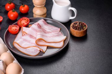 Gri bir tabakta koyu beton arka planda dilimlenmiş leziz taze pastırma. Lezzetli besleyici bir kahvaltı hazırlıyorum.