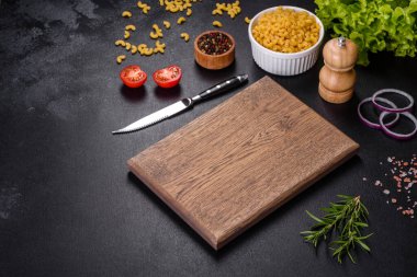 Koyu beton arka planda baharat ve otlarla dolu mutfak bıçağıyla ahşap bir kesme tahtası. Evde yemek pişirmek.