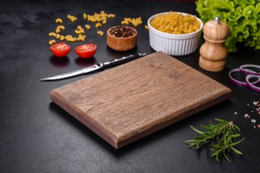 Koyu beton arka planda baharat ve otlarla dolu mutfak bıçağıyla ahşap bir kesme tahtası. Evde yemek pişirmek.