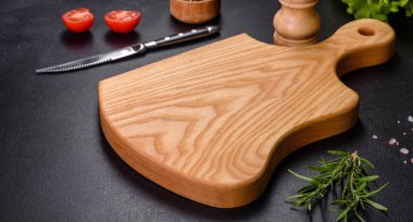 A wooden cutting board with a kitchen knife with spices and herbs on a dark concrete background. Cooking at home