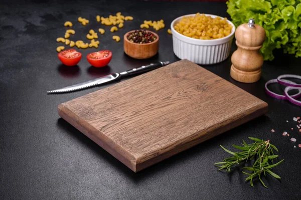 Koyu beton arka planda baharat ve otlarla dolu mutfak bıçağıyla ahşap bir kesme tahtası. Evde yemek pişirmek.