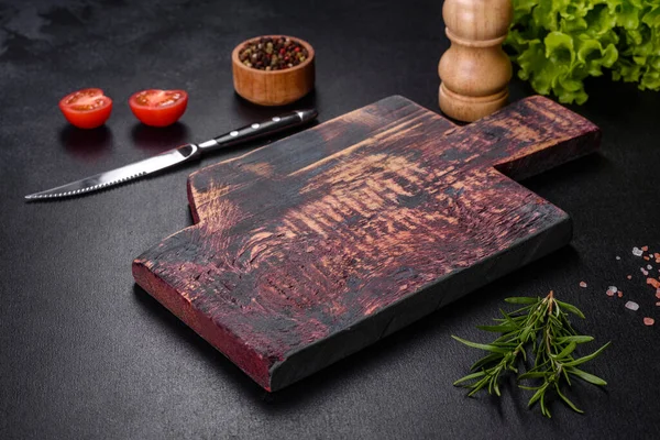 Koyu beton arka planda baharat ve otlarla dolu mutfak bıçağıyla ahşap bir kesme tahtası. Evde yemek pişirmek.