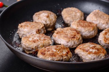 Kızartma tavasında kıymalı pirzola ve koyu beton zeminde baharatlar.