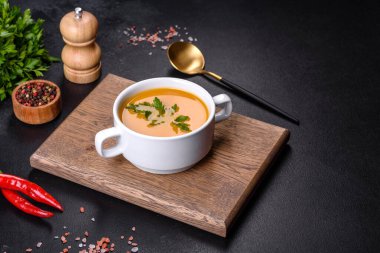 Lezzetli taze balkabağı püresi çorbası. Beyaz bir tabakta maydanozla süslenmiş. Koyu beton arka planda.