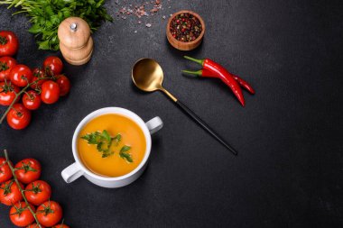 Lezzetli taze balkabağı püresi çorbası. Beyaz bir tabakta maydanozla süslenmiş. Koyu beton arka planda.