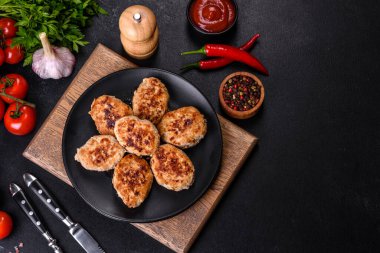 Kızartma tavasında kıymalı pirzola ve koyu beton zeminde baharatlar.