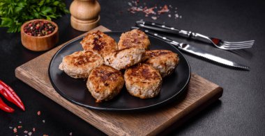 Kızartma tavasında kıymalı pirzola ve koyu beton zeminde baharatlar.