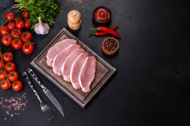 Ahşap bir kesme tahtasının üzerinde kesilmiş çiğ domuz eti, koyu beton bir arka planda.