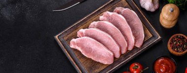 Ahşap bir kesme tahtasının üzerinde kesilmiş çiğ domuz eti, koyu beton bir arka planda.