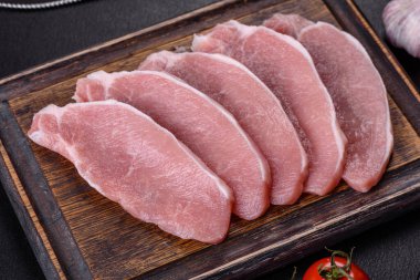 Ahşap bir kesme tahtasının üzerinde kesilmiş çiğ domuz eti, koyu beton bir arka planda.