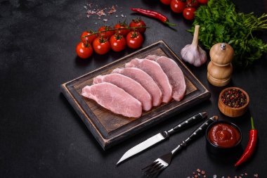 Ahşap bir kesme tahtasının üzerinde kesilmiş çiğ domuz eti, koyu beton bir arka planda.