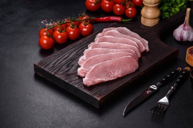 Ahşap bir kesme tahtasının üzerinde kesilmiş çiğ domuz eti, koyu beton bir arka planda.