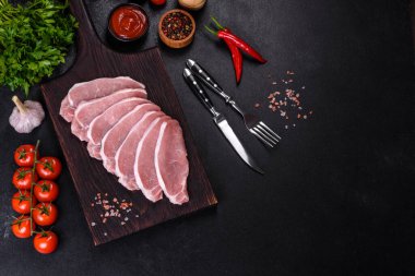 Ahşap bir kesme tahtasının üzerinde kesilmiş çiğ domuz eti, koyu beton bir arka planda.