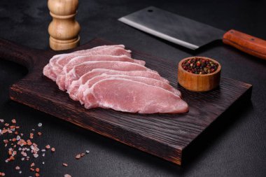 Ahşap bir kesme tahtasının üzerinde kesilmiş çiğ domuz eti, koyu beton bir arka planda.