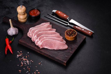 Ahşap bir kesme tahtasının üzerinde kesilmiş çiğ domuz eti, koyu beton bir arka planda.
