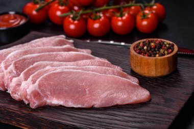 Ahşap bir kesme tahtasının üzerinde kesilmiş çiğ domuz eti, koyu beton bir arka planda.