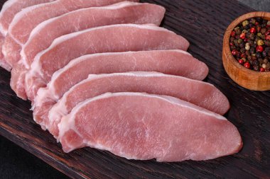 Ahşap bir kesme tahtasının üzerinde kesilmiş çiğ domuz eti, koyu beton bir arka planda.