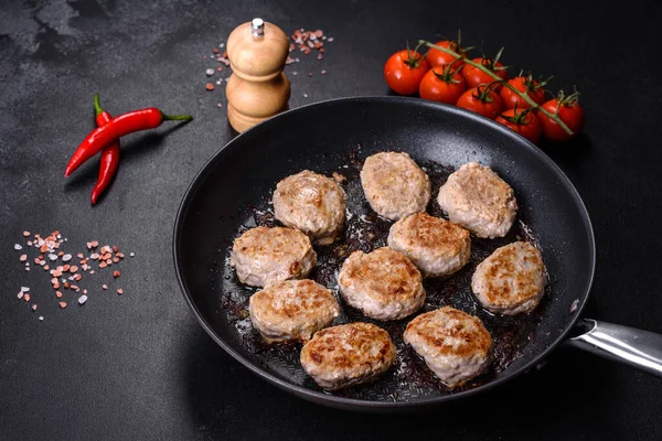 Kızartma tavasında kıymalı pirzola ve koyu beton zeminde baharatlar.