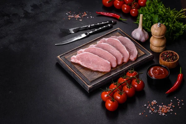 Ahşap bir kesme tahtasının üzerinde kesilmiş çiğ domuz eti, koyu beton bir arka planda.