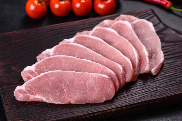 Ahşap bir kesme tahtasının üzerinde kesilmiş çiğ domuz eti, koyu beton bir arka planda.