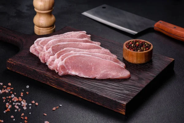 Ahşap bir kesme tahtasının üzerinde kesilmiş çiğ domuz eti, koyu beton bir arka planda.