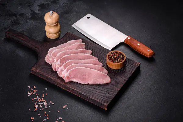 Ahşap bir kesme tahtasının üzerinde kesilmiş çiğ domuz eti, koyu beton bir arka planda.