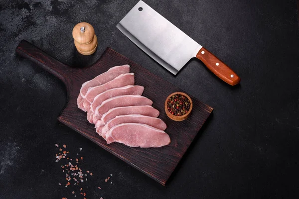 Ahşap bir kesme tahtasının üzerinde kesilmiş çiğ domuz eti, koyu beton bir arka planda.