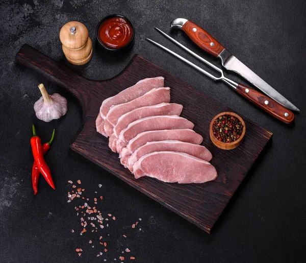 Ahşap bir kesme tahtasının üzerinde kesilmiş çiğ domuz eti, koyu beton bir arka planda.