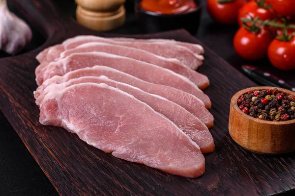 Ahşap bir kesme tahtasının üzerinde kesilmiş çiğ domuz eti, koyu beton bir arka planda.