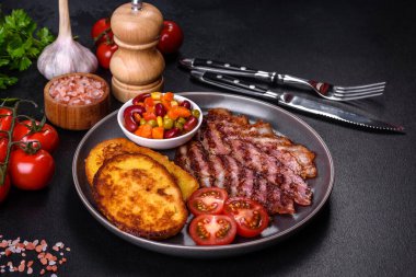 Lezzetli ızgara pastırma dilimleri, baharatlı, tuzlu, sebzeli ve çimento kaplı arka planda kızartılmış yumurta ve kızarmış ekmek.