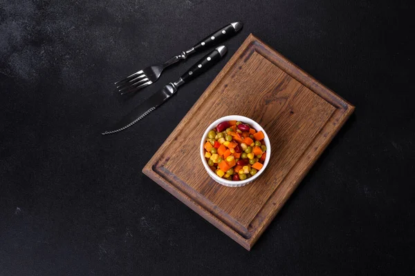 Kesilmiş sebze, kırmızı biber, mısır ve bezelye karışımı koyu beton bir arka planda.