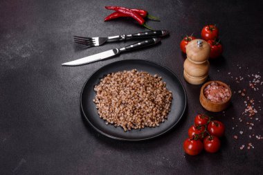 Lezzetli taze karabuğday lapası. Siyah bir tabakta sebze ve baharatlarla birlikte. Koyu beton arka planda.