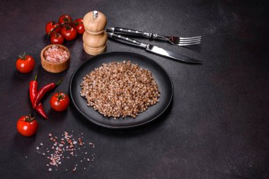 Lezzetli taze karabuğday lapası. Siyah bir tabakta sebze ve baharatlarla birlikte. Koyu beton arka planda.