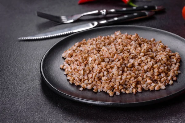 Lezzetli taze karabuğday lapası. Siyah bir tabakta sebze ve baharatlarla birlikte. Koyu beton arka planda.