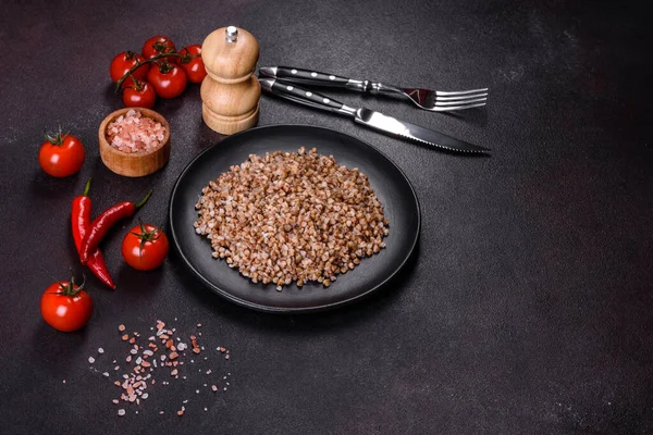 Lezzetli taze karabuğday lapası. Siyah bir tabakta sebze ve baharatlarla birlikte. Koyu beton arka planda.