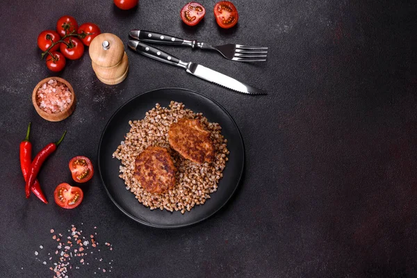 Lezzetli taze karabuğday lapası. Siyah bir tabakta sebze ve baharatlarla birlikte. Koyu beton arka planda.