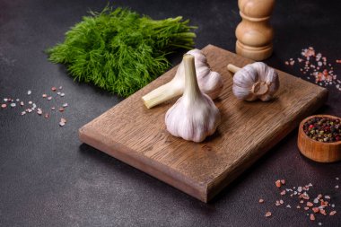 Tahta kesme tahtasının üzerinde koyu beton arka planda duran taze beyaz sarımsak kafalar. Evde yemek pişirmek.