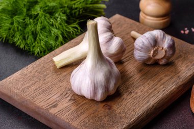 Tahta kesme tahtasının üzerinde koyu beton arka planda duran taze beyaz sarımsak kafalar. Evde yemek pişirmek.