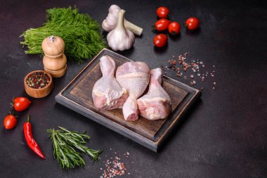 Ahşap bir kesme tahtasının üzerindeki baharatlı ve otlu çiğ tavuğun üç bacağı koyu beton arka planda. Evde yemek pişirmek.