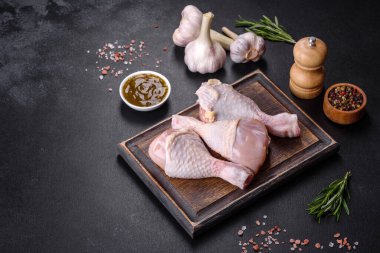 Ahşap bir kesme tahtasının üzerindeki baharatlı ve otlu çiğ tavuğun üç bacağı koyu beton arka planda. Evde yemek pişirmek.